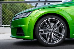 Close-up of a luxury green sports car with shining rims on a pavement.