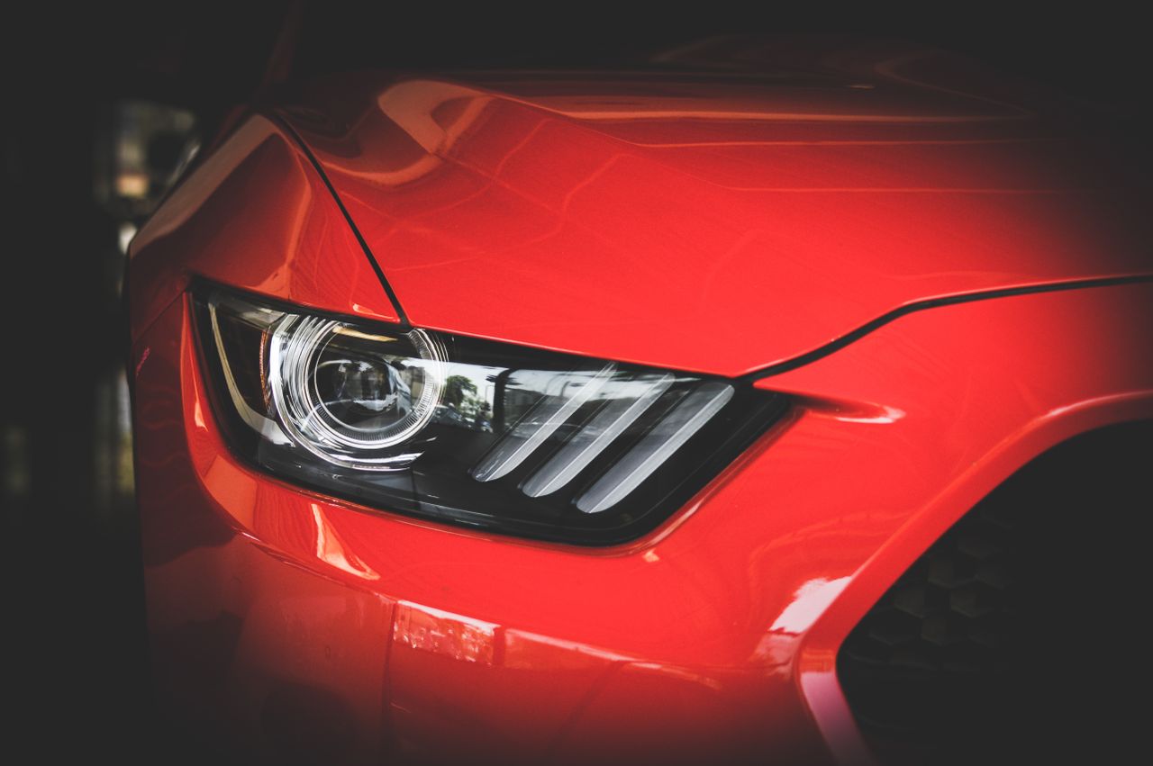 our-story-01 Detailed view of a red Ford Mustang's headlight showcasing sleek automotive design.