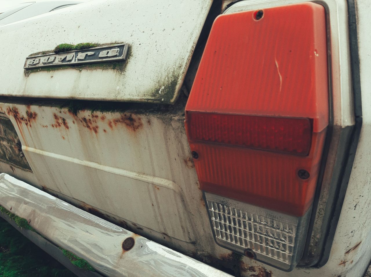 Close-up of a rusted vintage car with moss and an old taillight showing decay and neglect.